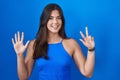 Hispanic woman standing over blue background showing and pointing up with fingers number eight while smiling confident and happy Royalty Free Stock Photo