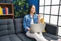 Hispanic woman using laptop at home pointing thumb up to the side smiling happy with open mouth Royalty Free Stock Photo