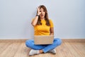 Hispanic woman using laptop sitting on the floor at home doing ok gesture shocked with surprised face, eye looking through fingers Royalty Free Stock Photo