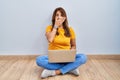 Hispanic woman using laptop sitting on the floor at home shocked covering mouth with hands for mistake Royalty Free Stock Photo