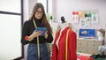 Hispanic woman using tablet in a tailor shop surrounded by mannequins and dressmaking tools Royalty Free Stock Photo
