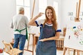 Hispanic woman wearing apron at art studio gesturing with hands showing big and large size sign, measure symbol Royalty Free Stock Photo