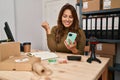 Hispanic woman working at small business using smartphone screaming proud, celebrating victory and success very excited with Royalty Free Stock Photo