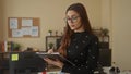 Hispanic woman writing notes on clipboard at modern office desk with computer and documents creating focused, professional work Royalty Free Stock Photo