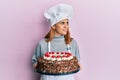 Hispanic young chef woman holding chocolate cake smiling looking to the side and staring away thinking Royalty Free Stock Photo