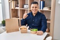 Hispanic young man eating take away food smiling with an idea or question pointing finger with happy face, number one