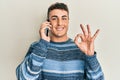 Hispanic young man having conversation talking on the smartphone doing ok sign with fingers, smiling friendly gesturing excellent Royalty Free Stock Photo