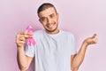 Hispanic young man holding pink cancer ribbon screaming proud, celebrating victory and success very excited with raised arm Royalty Free Stock Photo