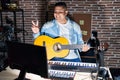 Hispanic young man playing classic guitar at music studio smiling with happy face winking at the camera doing victory sign with