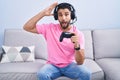 Hispanic young man playing video game holding controller sitting on the sofa crazy and scared with hands on head, afraid and Royalty Free Stock Photo