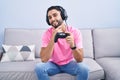 Hispanic young man playing video game holding controller sitting on the sofa looking confident at the camera smiling with crossed Royalty Free Stock Photo