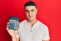 Hispanic young man showing calculator device thinking attitude and sober expression looking self confident