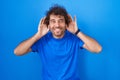 Hispanic young man standing over blue background trying to hear both hands on ear gesture, curious for gossip Royalty Free Stock Photo