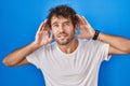 Hispanic young man standing over blue background trying to hear both hands on ear gesture, curious for gossip Royalty Free Stock Photo