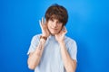 Hispanic young man standing over blue background trying to hear both hands on ear gesture, curious for gossip Royalty Free Stock Photo