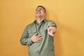 Hispanic young man standing over yellow background laughing at you, pointing finger to the camera with hand over body, shame Royalty Free Stock Photo