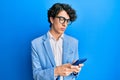 Hispanic young man using smartphone wearing business jacket thinking attitude and sober expression looking self confident Royalty Free Stock Photo
