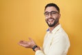 Hispanic young man wearing business clothes and glasses pointing aside with hands open palms showing copy space, presenting Royalty Free Stock Photo