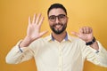 Hispanic young man wearing business clothes and glasses showing and pointing up with fingers number six while smiling confident Royalty Free Stock Photo