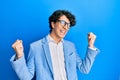 Hispanic young man wearing business jacket and glasses very happy and excited doing winner gesture with arms raised, smiling and Royalty Free Stock Photo