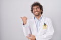 Hispanic young man wearing doctor uniform smiling with happy face looking and pointing to the side with thumb up Royalty Free Stock Photo