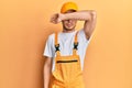 Hispanic young man wearing handyman uniform covering eyes with arm, looking serious and sad