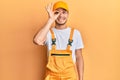 Hispanic young man wearing handyman uniform doing ok gesture with hand smiling, eye looking through fingers with happy face Royalty Free Stock Photo