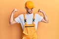 Hispanic young man wearing handyman uniform showing arms muscles smiling proud