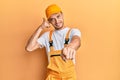 Hispanic young man wearing handyman uniform smiling doing talking on the telephone gesture and pointing to you Royalty Free Stock Photo