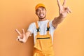 Hispanic young man wearing handyman uniform smiling with tongue out showing fingers of both hands doing victory sign Royalty Free Stock Photo