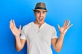 Hispanic young man wearing summer hat celebrating victory with happy smile and winner expression with raised hands Royalty Free Stock Photo