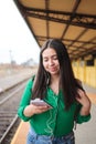 Hispanic young woman browsing social media on her smart phone, in a train station. Copy space