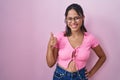 Hispanic young woman standing over pink background wearing glasses doing happy thumbs up gesture with hand Royalty Free Stock Photo