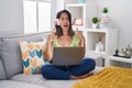 Hispanic young woman using laptop at home amazed and surprised looking up and pointing with fingers and raised arms Royalty Free Stock Photo