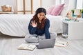 Hispanic young woman using laptop sitting on the floor at the bedroom looking positive and happy standing and smiling with a Royalty Free Stock Photo