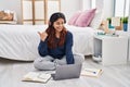 Hispanic young woman using laptop sitting on the floor at the bedroom pointing thumb up to the side smiling happy with open mouth Royalty Free Stock Photo