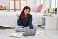 Hispanic young woman using laptop sitting on the floor at the bedroom smiling happy pointing with hand and finger to the side Royalty Free Stock Photo