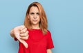 Hispanic young woman wearing casual red t shirt looking unhappy and angry showing rejection and negative with thumbs down gesture