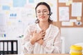 Hispanic young woman working at the office wearing headset and glasses smiling with hands on chest, eyes closed with grateful Royalty Free Stock Photo