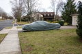 Historic antique muscle car in the driveway of a suburban house completely covered with a gray car protection cover.