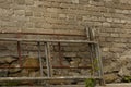 An old masonry wall made of bricks and stones and construction scaffolding lying next to it.