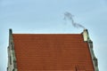 A historic building with a roof made of red tiles and a smoking chimney