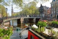 Historic buildings along Prinsengracht canal with Westerkerk Church clock tower in the background and colorful flowers and plants