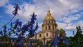 Historic Les Invalides dome in Paris, France with majestic golden cupola viewed through a sea of flowers with blue blossom. Royalty Free Stock Photo