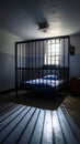 Historic prison cell with a caged bed and light from a barred window casting long shadows on the floor Royalty Free Stock Photo