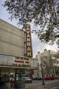 The Historic Savannah Theatre with a tall red neon sign with lush green trees, tall black light posts, cars parked