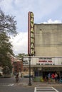 The Historic Savannah Theatre with a tall red neon sign with lush green trees, tall black light posts, cars parked