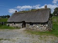 historic stone bricked house with thatch roof . in the background blue skies, white clouds and green grass in scotland .