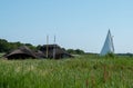 Historic thatched boathouses amongst the green reeds on Hickling Broad, east of Norwich, in Norfolk UK. Sailing boat on right.