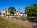 Historic white buildings with brick chimnes, a walk path and wodden fence with blue sky in Williamsburg, Virginia